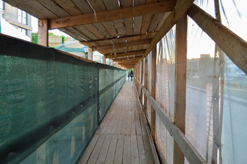large building walkway made of wood. fabric material on the sides. protection of pedestrians from construction debris. creation of an alternative pedestrian crossing. people are walking ahead