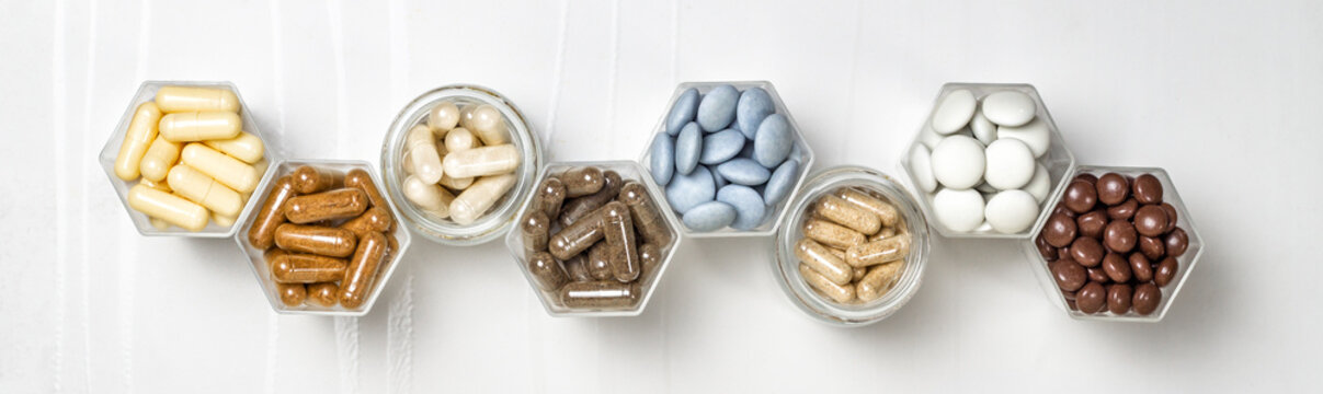 Various capsules and pills with dietary supplements or medicines in hexagonal jars
