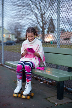 Preteen girl wearing roller skates using smartphone while seated on a bench in the park