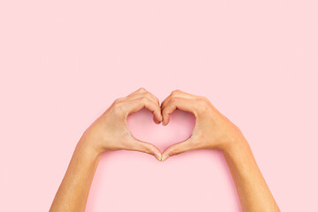 Manos de mujer haciendo una forma de corazón sobre fondo rosa pastel liso y aislado. Vista superior y de cerca. Copy space - obrazy, fototapety, plakaty