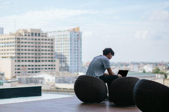 Young asian man working on laptop near pool with city in background
