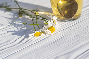 White wooden background in retro style. On it is a glass mug in which chamomile tea is brewed. Copy...