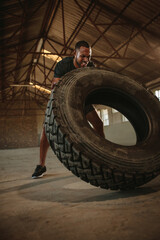 Fototapeta na wymiar Man doing tire flipping workout at empty warehouse