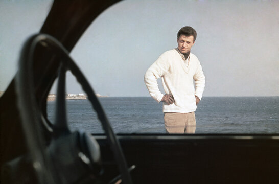 1969. Man standing outside his car