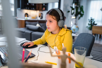 The preteen girl is studying online via the internet on tablet while sitting on a desk at home...