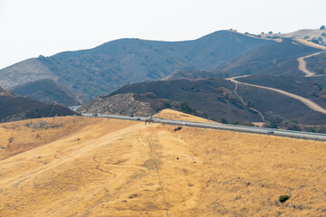 Freeway road with cars crossing the the San Luis Reservoir valleys during dry and hot season, San Luis Creek in the eastern slopes of the Diablo Range of Merced County, California. USA