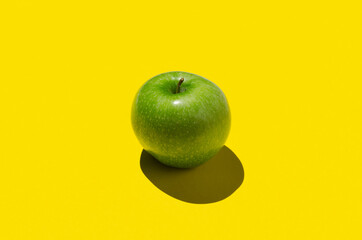 Green apple on a yellow background. Hard shadow.