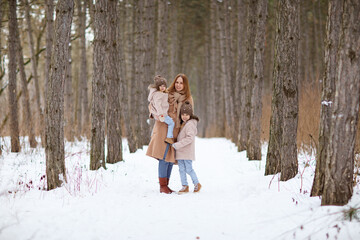 Fototapeta na wymiar mother with little daughters in a snowy winter forest. travel and recreation with children in winter. family walks in the fresh air during the new year holidays.