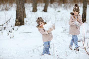 Fototapeta na wymiar little girls play in the winter forest and make snow balls for the snowman. walking in any weather. new year vacations. happy childhood.