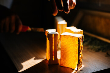 Close-up of hands of unrecognizable apiarist cutting honeycomb using knife while standing in dark bee house. Concept of bee agriculture.