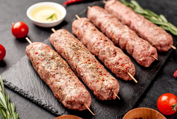 raw Lula kebab  on skewers with spices on a stone background 