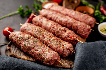 raw Lula kebab  on skewers with spices on a stone background 