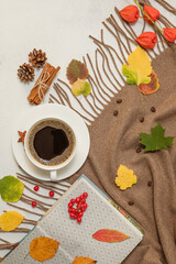 Autumn cozy composition. Coffee in a Cup, brown scarf, book, cinnamon sticks, fallen leaves on a white table. Selective focus.
