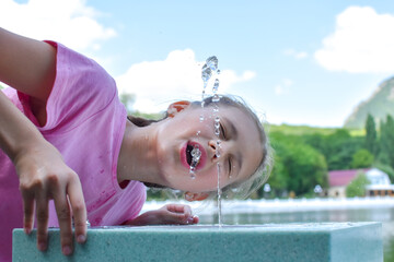 girl drinks spring water from fountain. Drinking mineral water in fresh air.