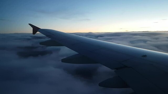 Beautiful descent of a passenger plane into the clouds. Low cloud cover during the flight. Thick Cumulus clouds on the background of the earth. Rainy weather. Bright dawn. Selective focus. 