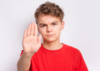 Teen boy doing stop sign with palm of hands, on gray background. Beautiful caucasian teenager...