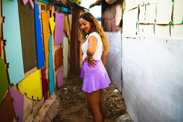 Chica joven con falda en una calle estrecha de un barrio pobre de favela en rio de janeiro brasil con muchos colores en sus casas casseria de ossio san fernando sur de españa