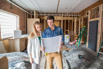 Caucasian couple reading blueprints at construction site