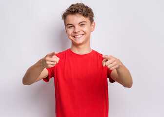 Portrait of happy teen boy pointing fingers at camera. Cute smiling child in red t-shirt choose you, on grey background. Laughing child having fan. - 380000259