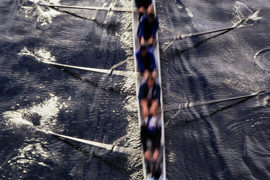 Competitive crew racers rowing scull boat, blurred motion