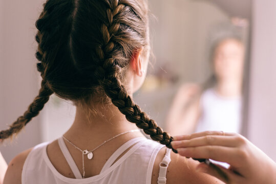 teen girl braiding hair in mirror