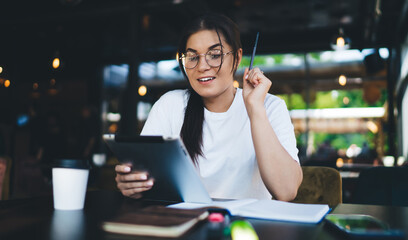 Skilled caucasian woman in eyewear for vision correction reading news from social networks via touchpad,pretty female blogger searching information and communicating via application on digital tablet
