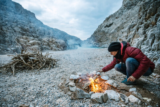 young woman with red jacket making a campfire at a beautiful bea