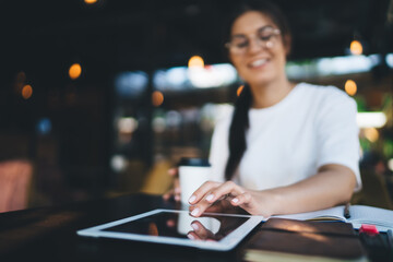 Selective focus on modern digital tablet lying on table, millennial woman 20s tapping and sending text messages via application on modern tablet connected to 4G internet share content in blog