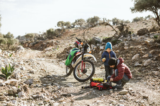 Mother And Son Having A Break On Rocky Off Road Pist With A Moto