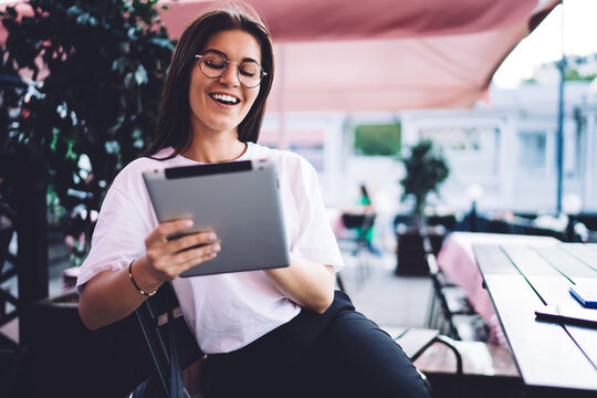 Smiling caucasian female blogger enjoying share content and publication in social networks, cheerful woman millennial in eyewear for vision correction laughing at funny videos on tablet during leisure