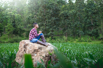 Young male sitting praying in corn field on a big stone. belief of agriculture concept.