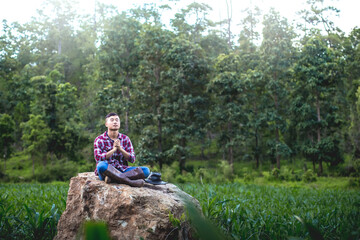 farmer male sitting on a big stone and praying in corn field. belief of agriculture concept.