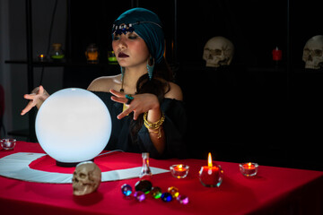 Young pretty Asian woman doing fortume telling witchcraft forecasting the future with crystal ball and Tarot card on red table with black background
