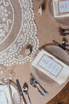 Top-down view of a menu resting on a crystal plate, set against a hessian and lace-covered dining table