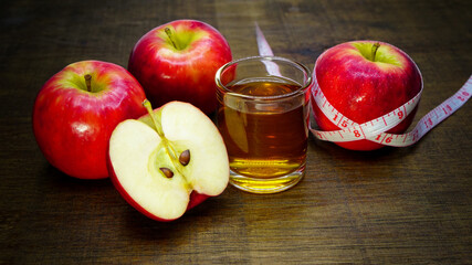 Apple cider vinegar in a glass with apples and a measuring tape on a wooden background.