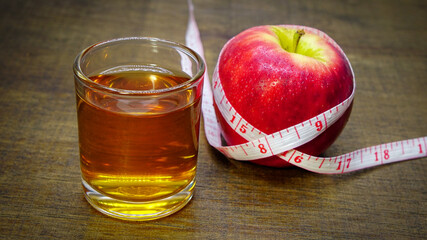 Apple cider vinegar in a glass with apples and a measuring tape on a wooden background.	