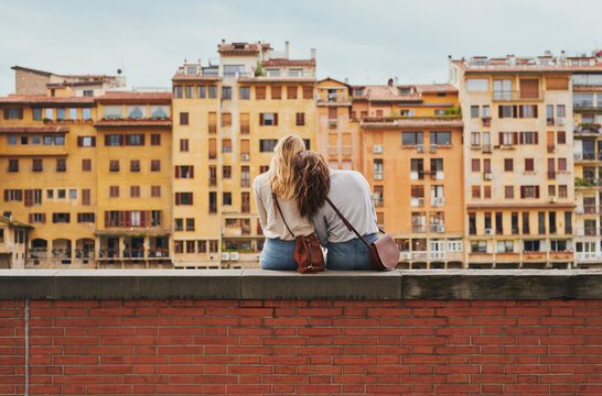Two tourist girl friends relaxing on historical bridge in Floren