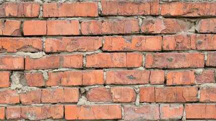 fragment of a dilapidated brick wall with a rough texture of old broken blocks and uneven layers of gray dried concrete mortar