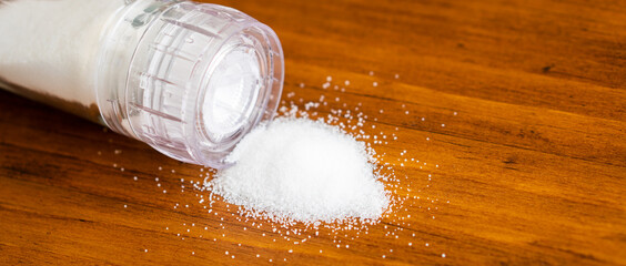 Close up white natural organic sea salt powder flake cook ingredient in grinder bottle glass on vintage rustic black kitchen wooden table