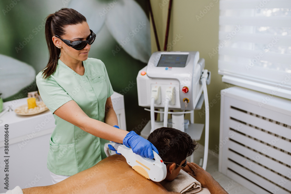 Wall mural Young good looking man getting hair removal cosmetology procedure on face at cosmetic beauty spa clinic.