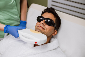 Young good looking man getting facial hair removal cosmetology procedure at cosmetic beauty spa...