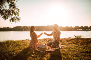 A cute blonde woman in a pastel pink dress and a caucasian man drinking white wine on the beach at...