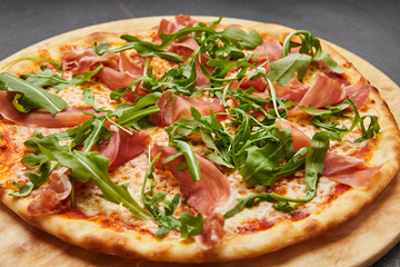 Delicious Italian Pizza with Parma ham and arugula, mozzarella cheese on dark background