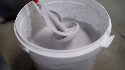 The white paint is mixed in a bucket with a drill. Drill paddle mixer on a bucket with white paint,...