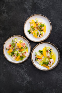 three plates with raw fish, celery, orange and herbs