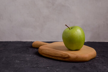 Green apple on a wooden board, gray background. Copy space