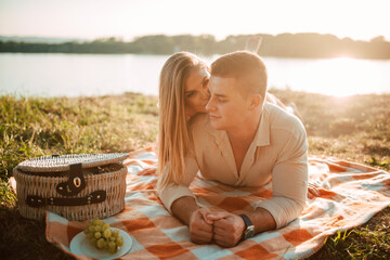 A portrait of a caucasian man and a blonde woman lying on a blanket at a picnic by the river. Romantic happy loving couple in the sunset