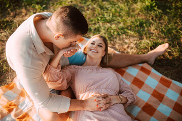 Fototapeta premium A beautiful blonde caucasian woman in a dress is lying on a blanket next to her man. Romantic loving couple on a picnic by the river