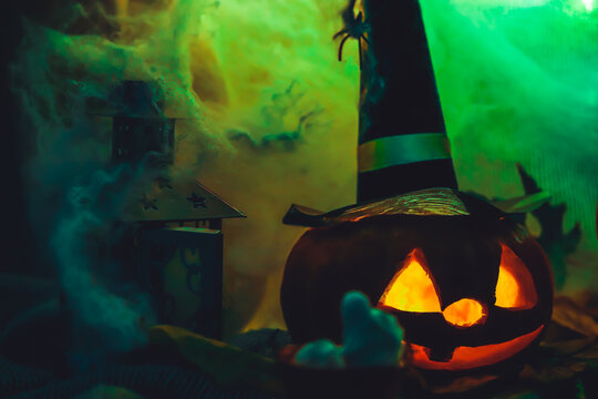 Halloween party carved pumpkin in witch black hat spooky scary face with light and lantern in web on dark neon