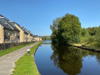 Fototapeta na wymiar Looking along the Rochdale Canal, with a footpath, new housing, and a vivid blue sky near, Stubley, Rochdale, UK